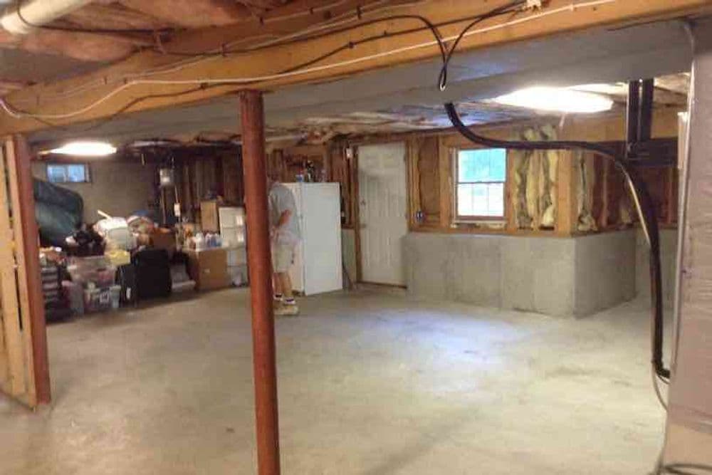 Spacious unfinished basement with storage areas, concrete floor, and white appliances.